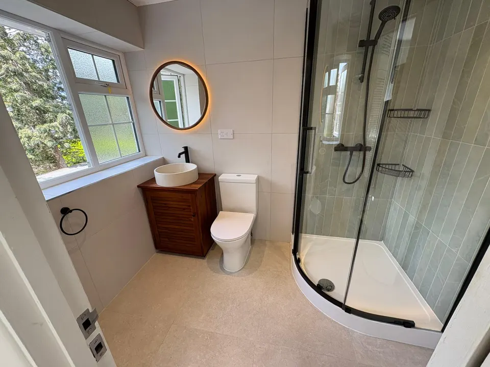 Completed bathroom with glass shower, timber vanity and illuminated round mirror